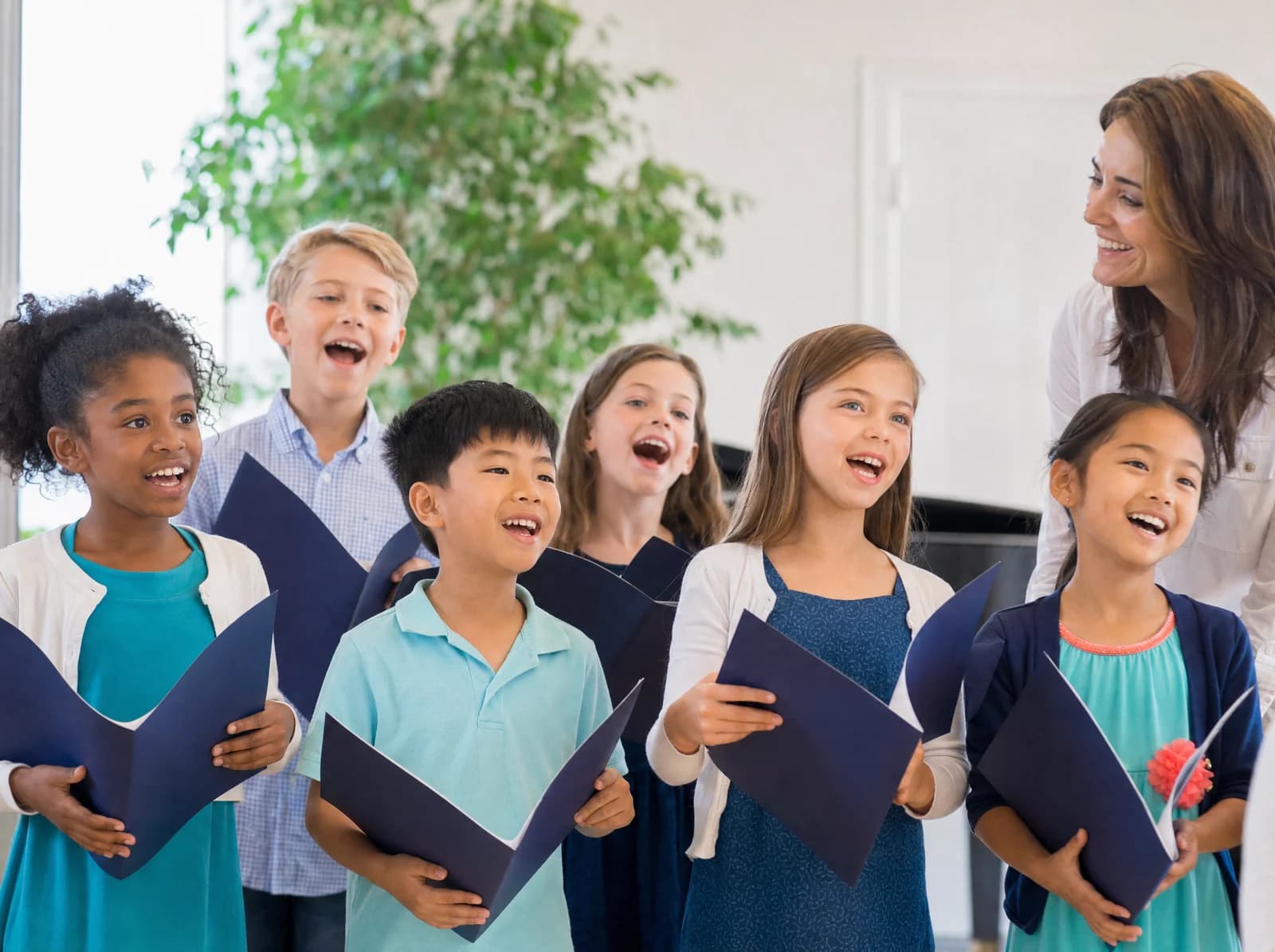 A children's choir singing together, holding song folders in a bright hall.